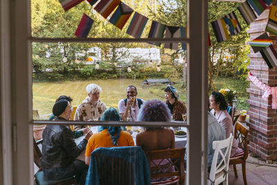 Friends of lgbtq community enjoying during dinner party in back yard seen through window