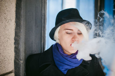 Close-up of woman exhaling smoke by wall