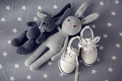 Two grey knitted toy rabbit and children's white shoes are on grey background with stars