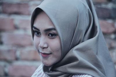 Close-up of woman wearing hijab against brick wall