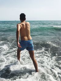 Shirtless man running in sea against sky