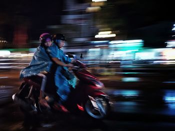 Women riding motorcycle on road in defocused city during rainy season