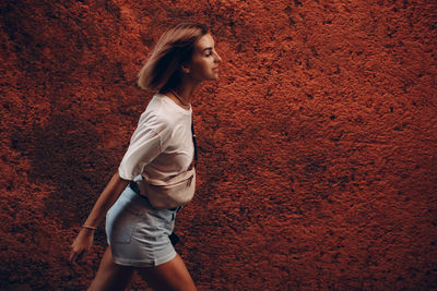 Side view of young woman standing against wall