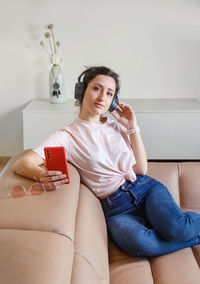 Young women listening to music with headphones with cell phone in hand while sitting 