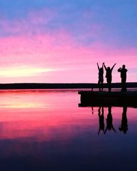 Silhouette people standing by lake against sky during sunset