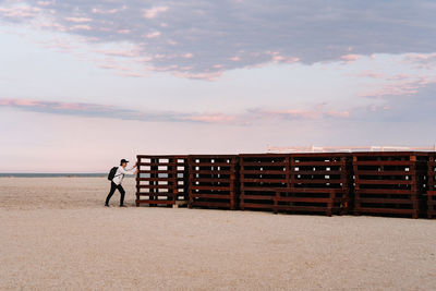 Man standing on shore against sky during sunset