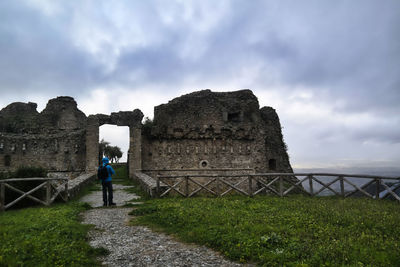 Man standing in front of historical building against cloudy sky