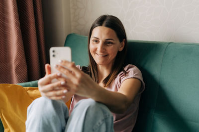 A woman in the forties sitting on the couch communicates by video call in a mobile phone.