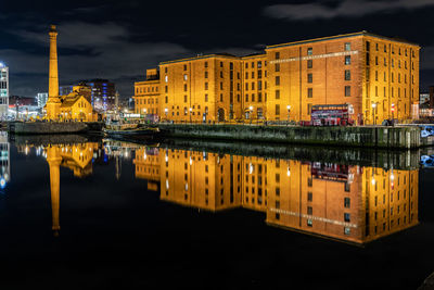 Illuminated buildings by dockside against sky in city at night