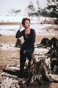 Thoughtful woman sitting on tree stump at beach