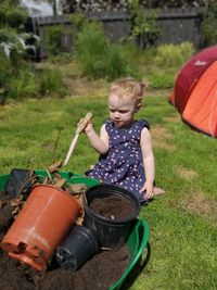Cute baby girl holding gardening tool by pots in yard