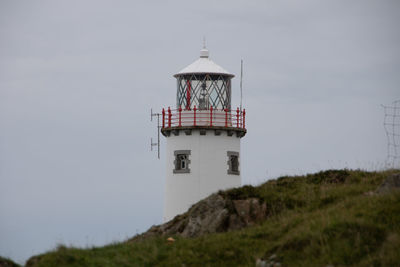 Lighthouse on field by building against sky