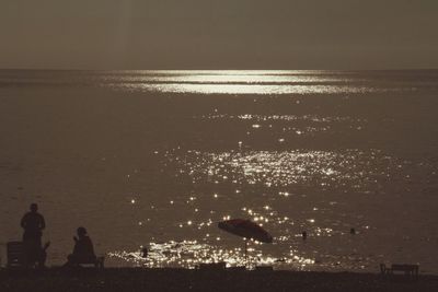 Silhouette people standing on beach against sky during sunset