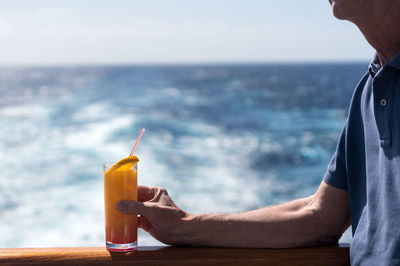 Midsection of man holding drink glass by sea