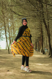 Portrait of young woman standing against trees