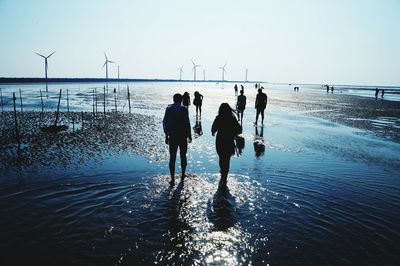 People at beach by wind turbines against clear sky