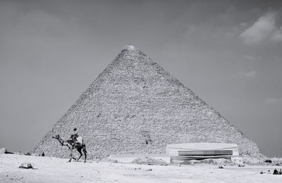 Man riding camel against pyramid at desert