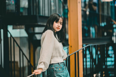 Young woman looking away while standing against railing