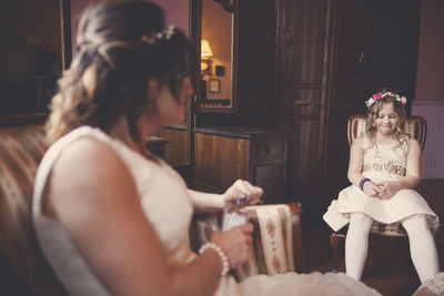 Bride and flower girl sitting on chairs at home