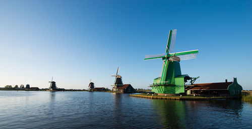 Traditional windmills by canal at zaanse schans against clear sky