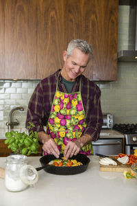 Smiling mature man preparing pizza in kitchen at home