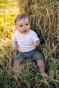 Gay boy kid blonde in white tank top sitting on a field of hay next to the stack during sunset