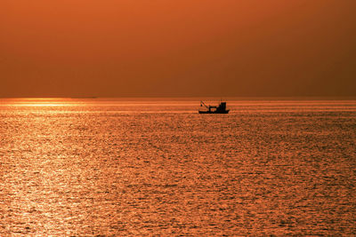 Silhouette boat sailing on sea against orange sky