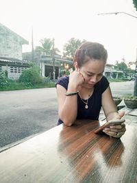 Young woman using mobile phone while sitting in city
