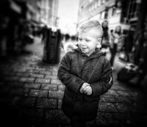 Cute boy looking away while standing on street in city