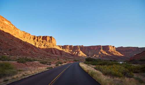 Road leading towards mountains against clear sky