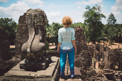 Rear view of woman standing by old statue at temple against sky