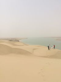 Mid distance view of men at desert with lake in background against clear sky