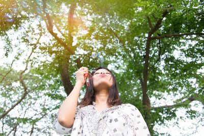 Low angle portrait of woman against trees