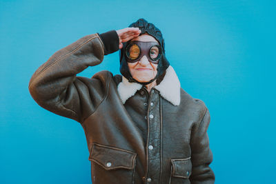 Portrait of senior woman wearing glasses while saluting against blue background
