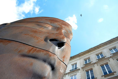 Low angle view of sculpture and building against sky on sunny day