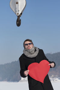 Man holding paper heart shape while standing outdoors