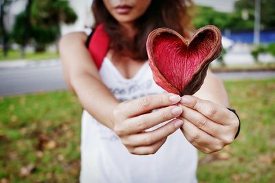 Midsection of woman holding heart shape plant in park