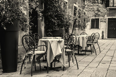 Empty chairs and tables on sidewalk by building