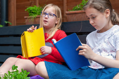 Two school age girls sitting together in garden and doing homework.