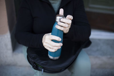 Senior woman hands holding bottle at doorway of house