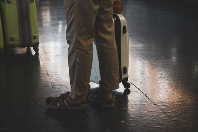 Low section of man with luggage standing on tiled floor at railroad station platform