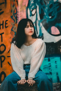 Portrait of beautiful woman standing against graffiti wall