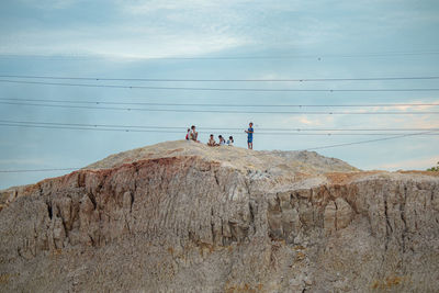 People on rocks by mountain against sky