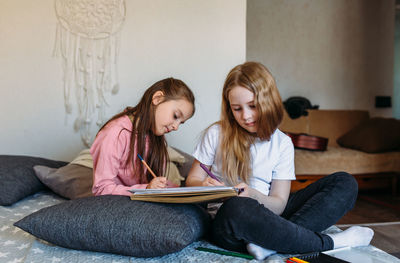 Two girls friends play at home, draw with pencils and felt-tip pens and have fun