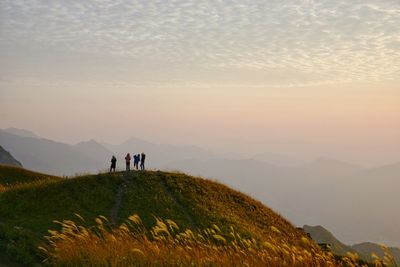 People standing on mountain against sky during sunset