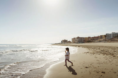 Rear view of little girl walking at beach against clear sky