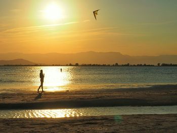 Person flying kite on beach by sea against sky during sunset