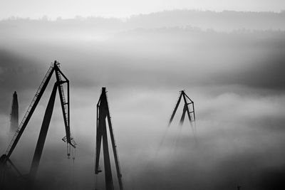 Cranes against sky in foggy weather