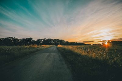 Road amidst field against sky during sunset