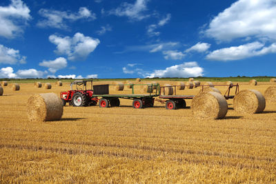 Tractor on field amidst hay bales against sky